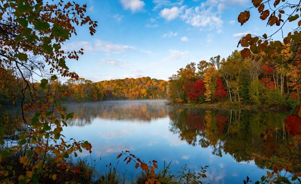 Lago calmo in autunno con alberi colorati riflessi nell’acqua, simbolo di silenzio interiore e vuoto creativo.